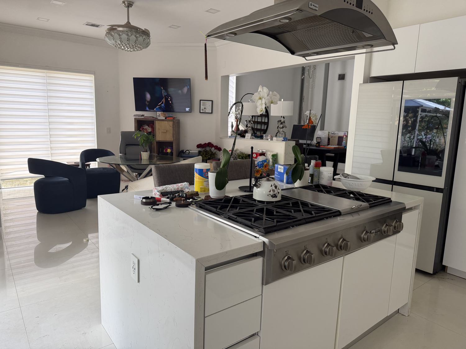 Open contemporary kitchen with waterfall quartz island, professional six-burner gas range and stainless hood, opening to the family room